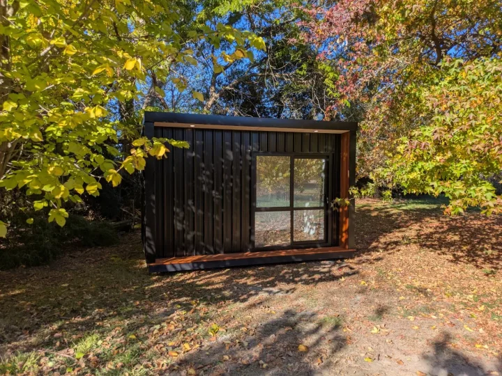 Black cabin with a kwila reveal under autumn trees