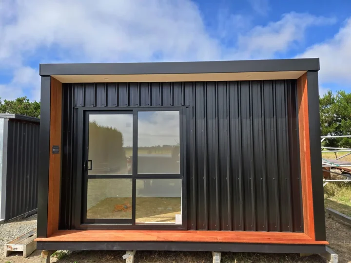 Black cabin seen front-on, framed in kwila, with a glazed sliding door