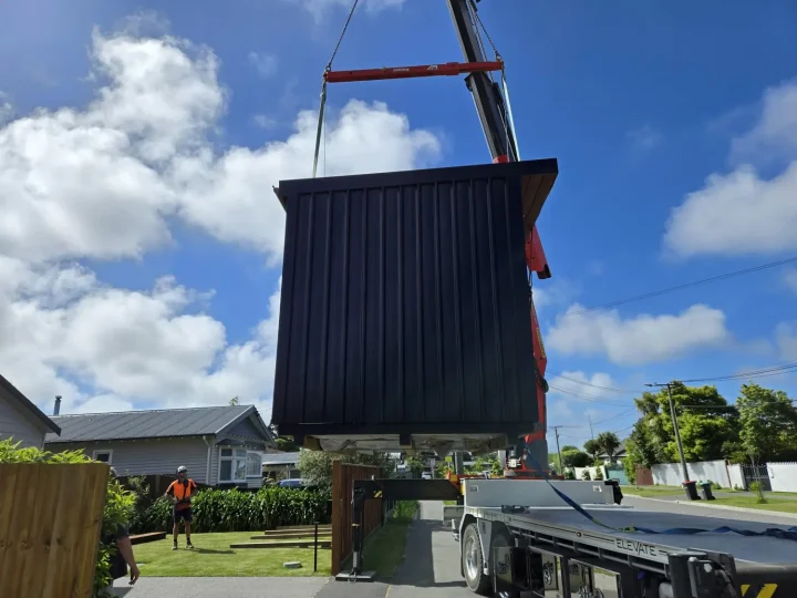 A cabin hanging from a crane, high above a garden fence