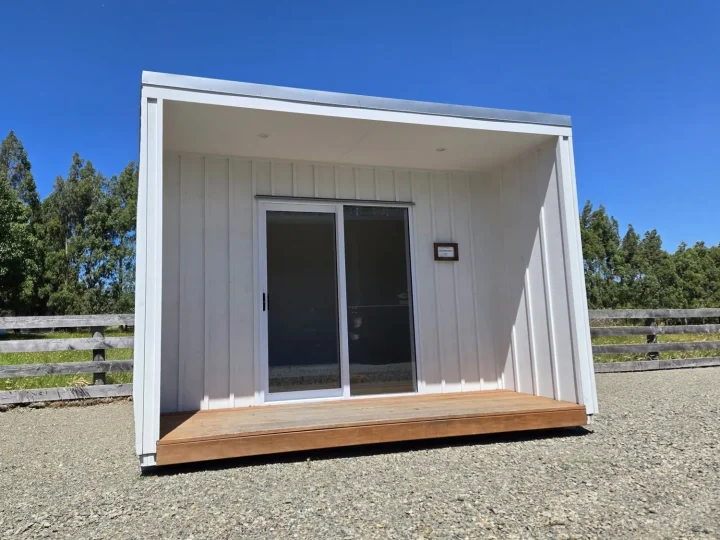 White cabin with a sliding door and a kwila deck under a blue sky