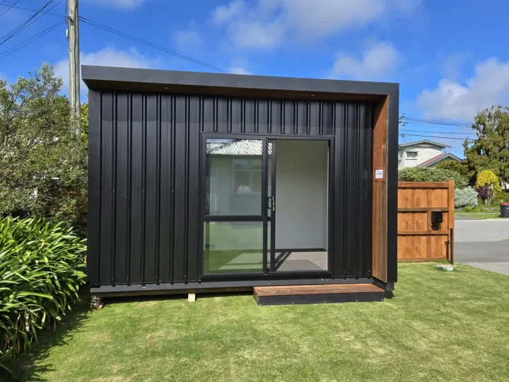 Black cabin sitting level on a lawn with its door open and a step in place
