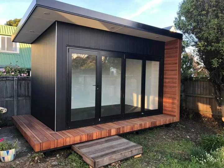 Black cabin with a kwila deck and steps in a back garden