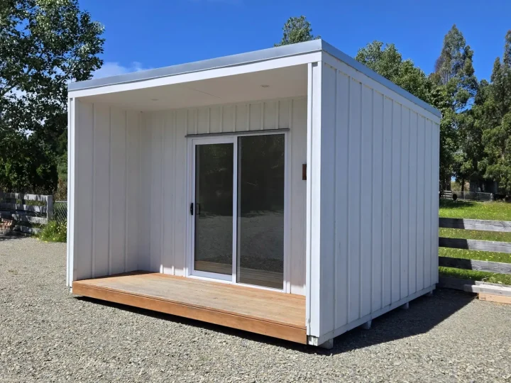 White cabin seen from an angle, with its deck and sliding door