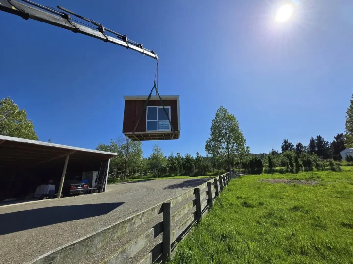 A kwila-fronted cabin swung over a paddock fence by crane