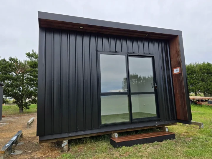 Black cabin on grass with a glazed sliding door and a step