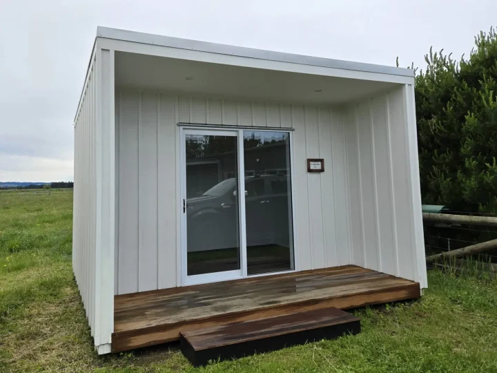 White cabin with a weathered kwila deck on grass