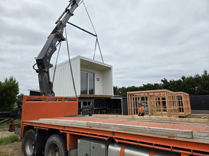 A white cabin being lifted off a truck deck by crane