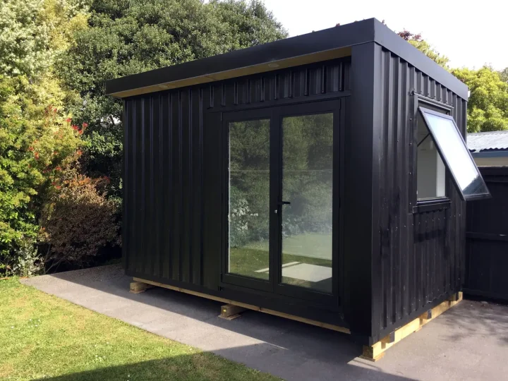 Black cabin with glazed doors and an awning window in a garden