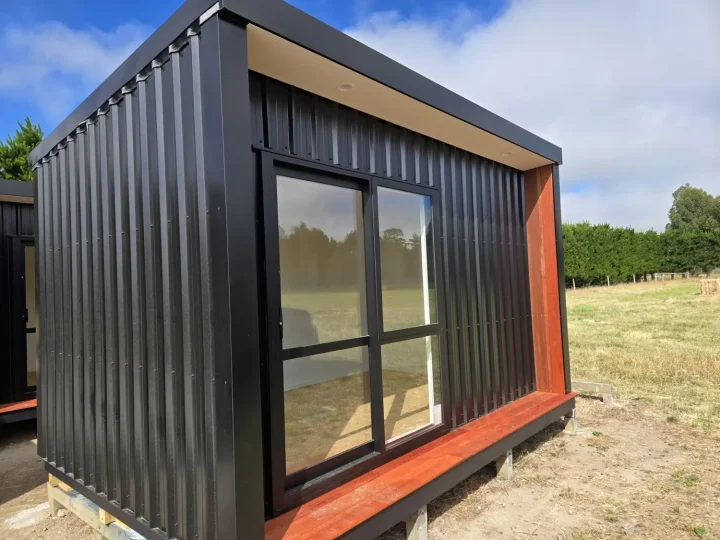 Black cabin seen from the corner, with its kwila frame and glazed door