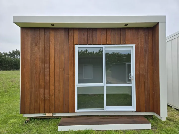 Kwila-fronted cabin seen front-on, with a white-framed sliding door and a step